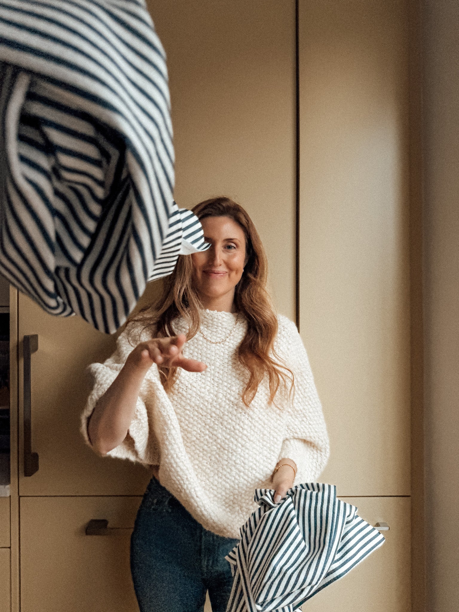 Woman in a kitchen holding the best striped tea towels, wearing a white sweater and blue jeans.